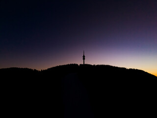 Sunset view of a communications tower on a mountain peak surrounded by trees in the evening sky