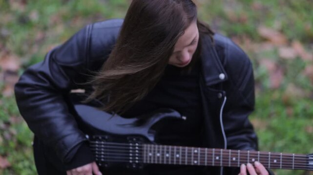 Young woman in a leather jacket, rock musician plays electric guitar outdoors