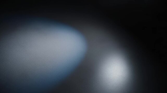 An out-of-focus frame shows two diffused light ovals on a dark gradient; a cool bluish blur on the left and a smaller white glow on the right create a quiet, abstract, cinematic mood.