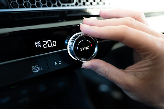 close-up of hand adjusting the dual climate control knob (AC air conditioning) in a modern car dashboard showing twenty degrees celsius on a digital display with sync function