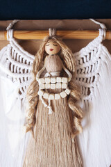 Naklejka premium Handmade macrame angel wall decoration with wooden beads and natural cotton cord. Boho craft guardian angel ornament hanging on wooden rod. Rustic handmade spiritual home decor symbol.