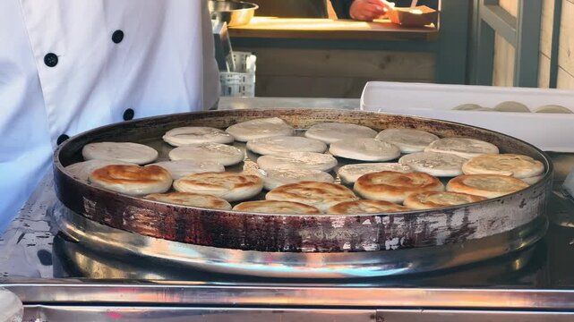 At the market, a cook carefully flips freshly cooked xian bing on a large round pan. Hot, crispy flatbreads and fresh Chinese street food.