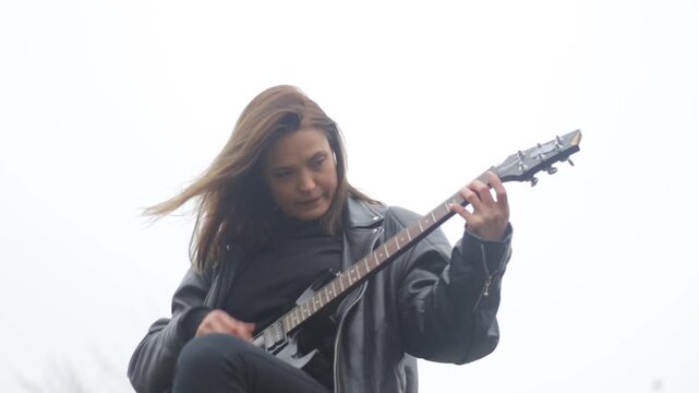 Young woman in a leather jacket, rock musician plays electric guitar outdoors