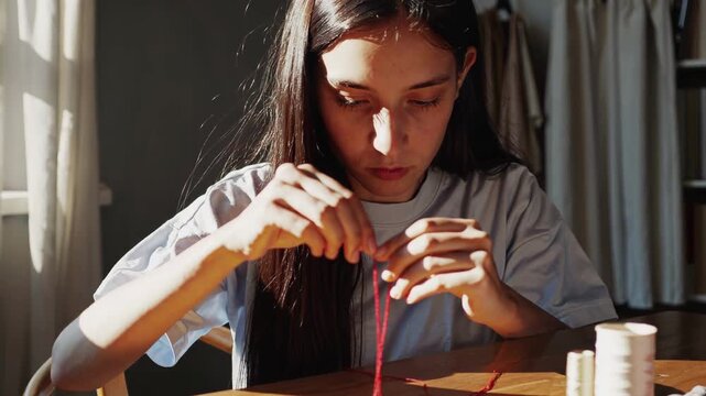 Young Woman Sewing At Sunlit Table Focused On Threading Needle, Hands Near Spool And Thimble, Warm Afternoon Light Through Window, Intimate Domestic Craft Scene Showing Patience And Precision
