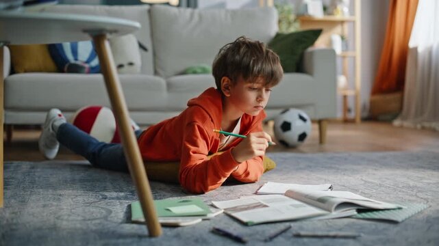 Attentive pupil flipping pages textbook making homework lying floor closeup.