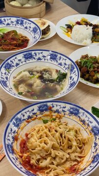 Close-up of Chinese cuisine dishes arranged on a dining table. Several plates with prepared meals are placed together for serving. Cafe, bistro or restaurant or dining setting. People eating