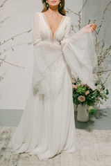 Fototapeta premium Woman in white dress stands in front of floral arrangement, showcasing bridal fashion in a soft light environment during a wedding event