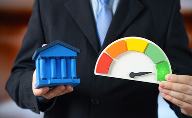 A man in a suit holds a bank and a performance scale showing the highest green level. High liquidity of bank assets and financial stability. Strong banking sector supports economic growth.
