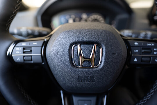 Detailed view of a modern honda steering wheel featuring the chrome honda logo emblem srs airbag cover and multifunction steering controls on black leather