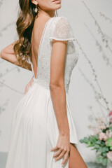 Fototapeta premium Woman wearing a white dress with a low back stands in front of floral decorations in a bright setting during a fashion shoot