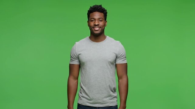 A young dark-skinned man wearing a light gray t-shirt standing against a solid green background with a friendly smile.