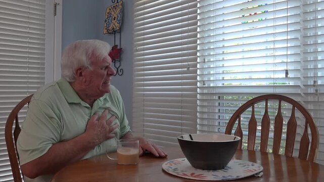 Man drinking coffee at kitchen table and looking out window when he appears to have a medical emergency, possibly heart attack.