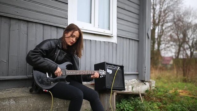 female rock musician in a leather jacket plays an electric guitar with an amplifier