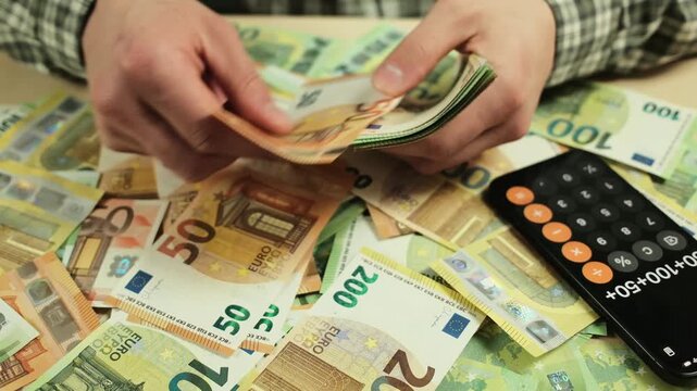 Hands counting euro banknotes on a table with scattered cash and a smartphone calculator. Concept of personal finance management, budgeting, saving money and financial planning