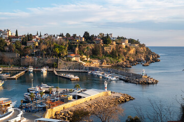 Obraz premium Panoramic view of Kaleici marina and the historic old town of Antalya with boats in the harbor and warm golden hour sunset light illuminating the Mediterranean coastline in southern Türkiye.