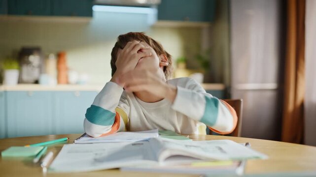 Bored schoolboy learning school subject doing homework home kitchen closeup.