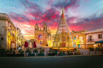 Magical Christmas tree and dramatic sunset over Marsaxlokk village square and historic church, Malta