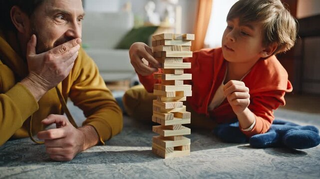 Attentive son building jenga tower with supportive dad lying home floor closeup