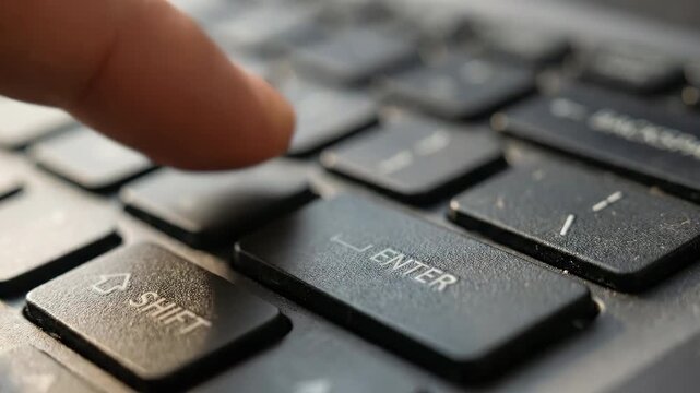 Finger pressing the enter key on a laptop keyboard close up shot.