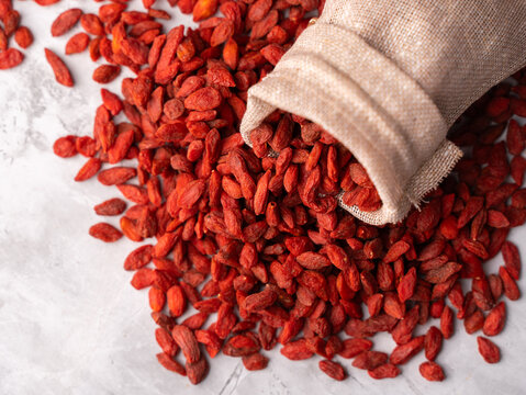 Dried Goji berries or Wolfberry scattered, vibrant red, in a wooden bowl on a textured background.