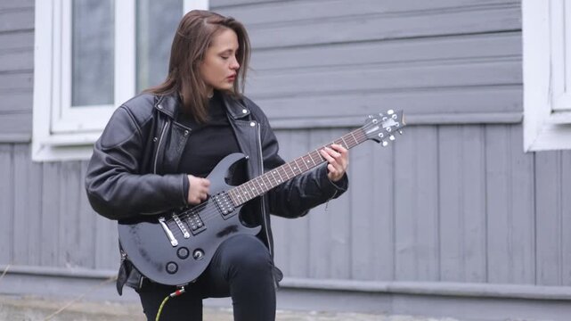 female rock musician in a leather jacket plays an electric guitar with an amplifier