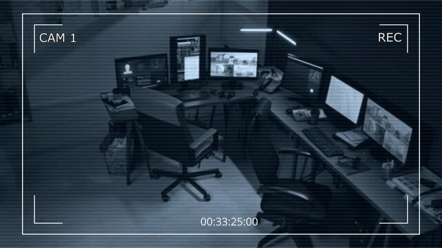 Black and white CCTV footage of police dispatchers desk with workstation equipped with multiple computers showing security camera feed and data, no people, high angle view