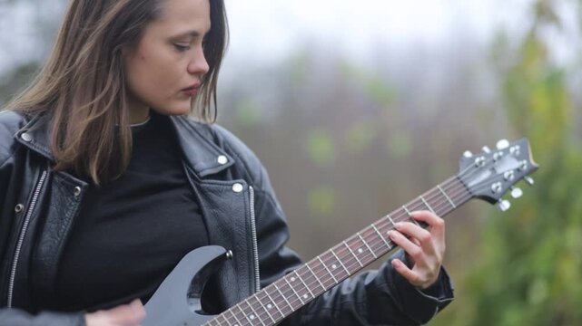 Young woman in a leather jacket, rock musician plays electric guitar outdoors