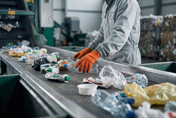 Fototapeta premium Recycling plant worker sorting plastic waste on conveyor belt