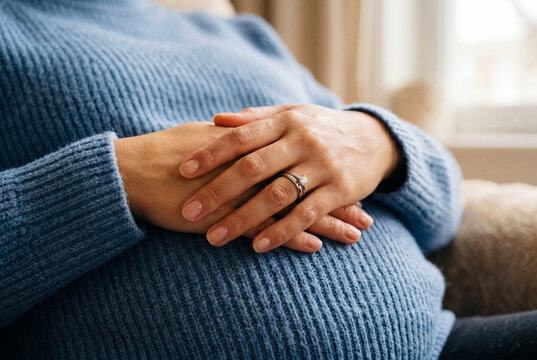 Pregnant woman hands on belly with wedding ring in blue sweater