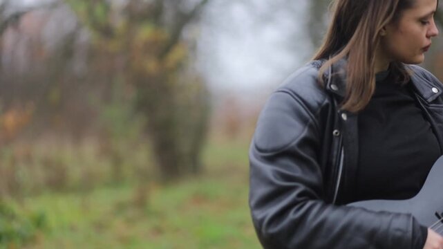 young female rock musician in a leather jacket plays an electric guitar outdoors
