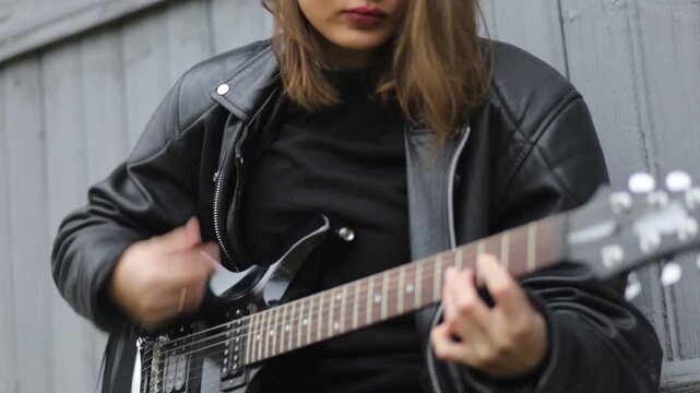 Young woman in a leather jacket, rock musician plays electric guitar outdoors