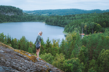 Active mature woman hiker enjoying a panoramic view of a Swedish lake. Lady standing on a cliff edge looking at Lake Stensj&ouml;n