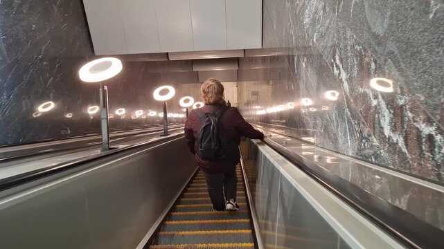 Passenger coming down a high-tech escalator in a contemporary subway hub. The perspective view showcases rhythmic ring-shaped lamps and polished metallic surfaces in a busy urban transit environment