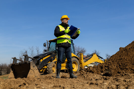 Site manager standing with documents in front of backhoe loader
