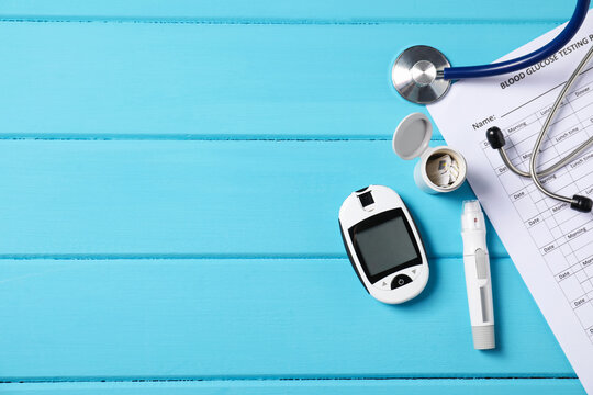 Diabetes. Digital glucometer, pen, test strips, stethoscope and record form on light blue wooden table, flat lay