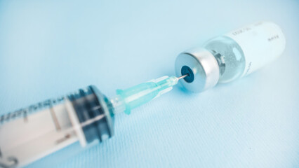 Close up syringe needle drawing vaccine from vial on blue background representing vaccination and pharmaceutical medicine