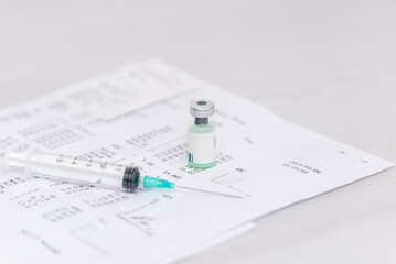 Fototapeta premium Vaccine vial and syringe lying on medical blood test document representing disease prevention and healthcare treatment concept