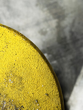 Close-up of a yellow painted concrete bollard edge against a blurred gray concrete background. Background texture