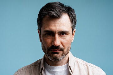Serious man with beard looking at camera, having intense gaze on blue background