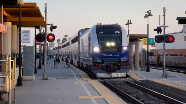 LOS ANGELES, CA, NOV 8, 2025: Amtrak Pacific Surfliner train arrives at Glendale station at dusk, headlights on, passengers waiting on the platform, red signals lit