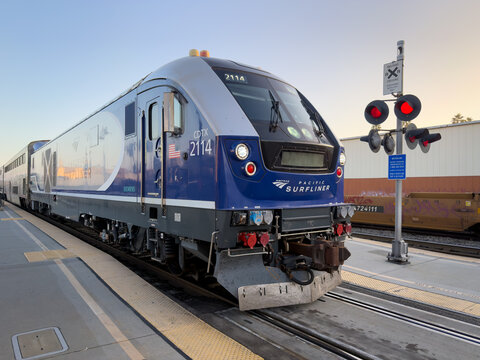 LOS ANGELES, CA, NOV 8, 2025: Close-up of Amtrak Pacific Surfliner train locomotive at dusk, showing red crossing signals, bold blue livery and Siemens branding