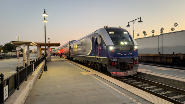 LOS ANGELES, CA, NOV 29, 2025: Amtrak Pacific Surfliner train at Glendale station at dusk, passengers boarding, palm trees silhouetted, headlights illuminating the platform