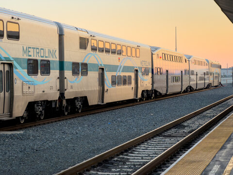 LOS ANGELES, CA, NOV 29, 2025: Side profile of Metrolink bi-level passenger train coaches at golden hour, warm orange sky reflecting off stainless steel car bodies, Union Station, Downtown