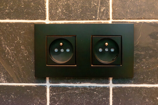 Modern minimalist double black electrical outlet socket installed on a dark grey natural stone tile wall.