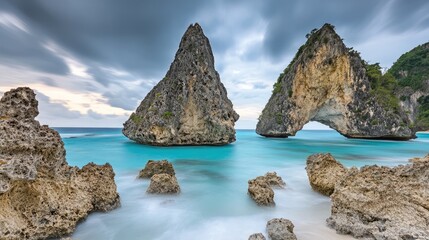 Naklejka premium Dramatic rock formations, turquoise ocean, cloudy sky, tropical beach; travel, nature