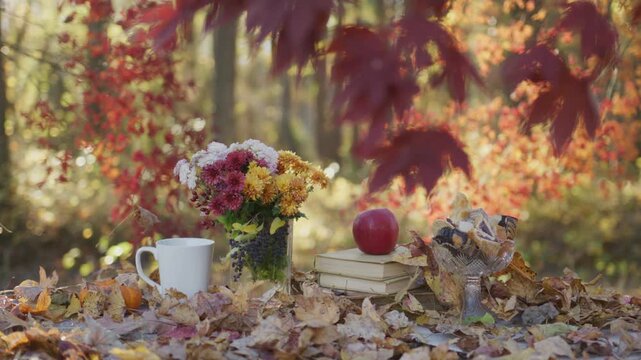 Cozy autumn table in warm colors. Fall leaves around a cozy setup. Autumn treats on rustic table. Warm fall still life outdoors. Cozy table with autumn bouquet.