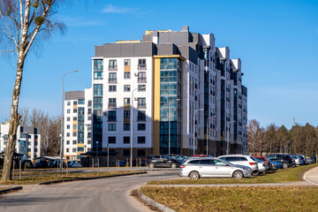 Fototapeta premium Modern apartment building with parked cars along residential street under clear blue sky in urban neighborhoo