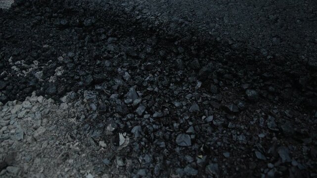 Slow motion video of the cross-section of a new road in Siska, Ljubljana, reveals the distinct layers of construction: a base of compacted grey aggregate and a thick, fresh layer of black asphalt.