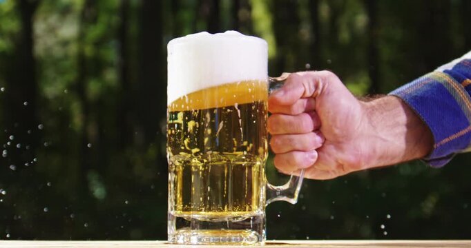 Golden craft beer poured outdoors. Beer splash against green nature background. Pouring amber ale in nature. Brewed beer with bubbles and foam. Craft brewery lager beer on summer day.