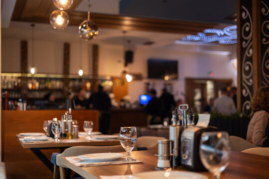 elegant restaurant interior with warm ambient lighting, blurred background, and perfectly set wooden tables with glassware, creating a cozy dining atmosphere